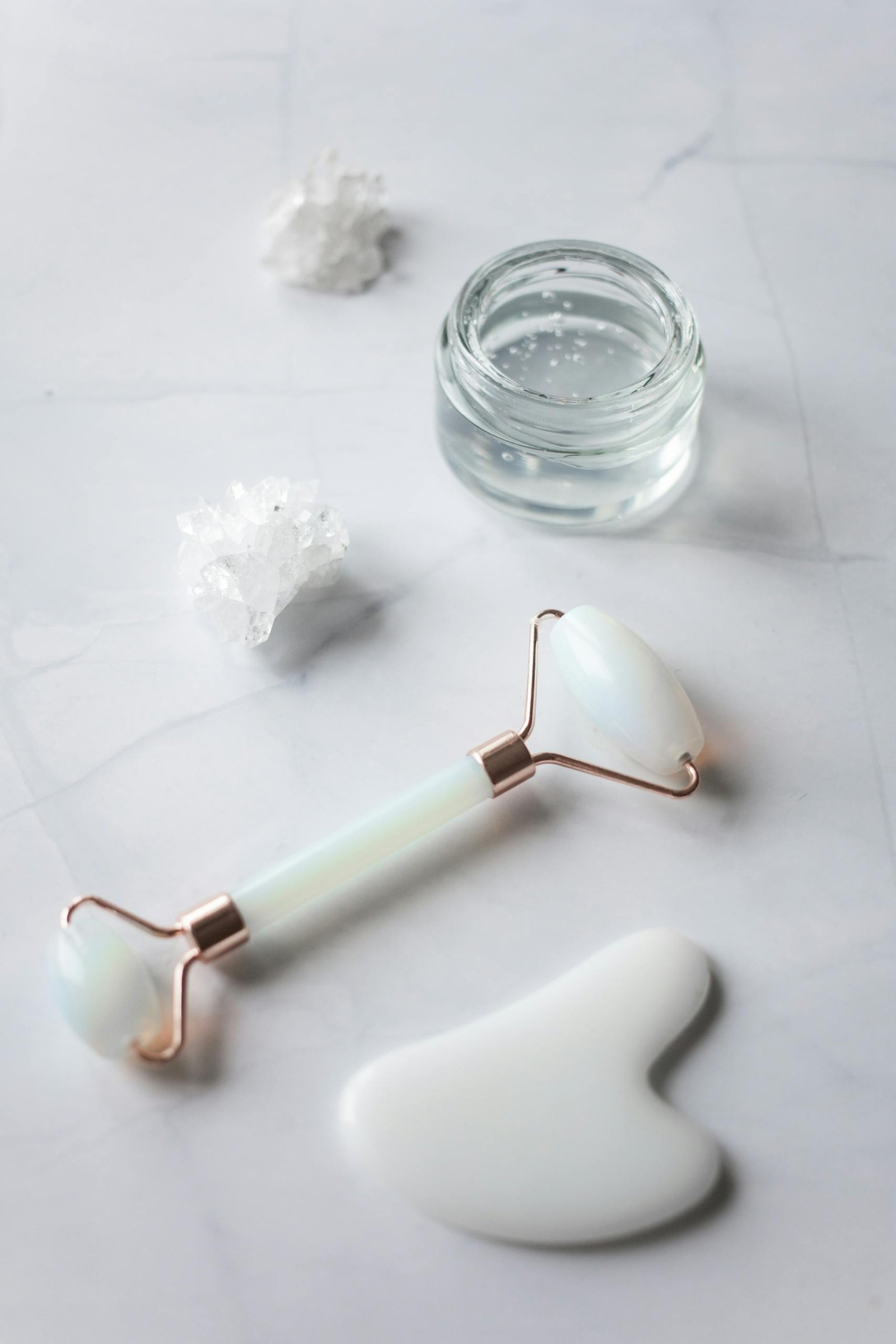 Jade roller, gua sha, and cream jar on elegant marble for skincare routine.