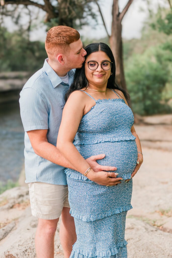 Husband kisses wife on the forehead while they lay hands on her pregnant stomach