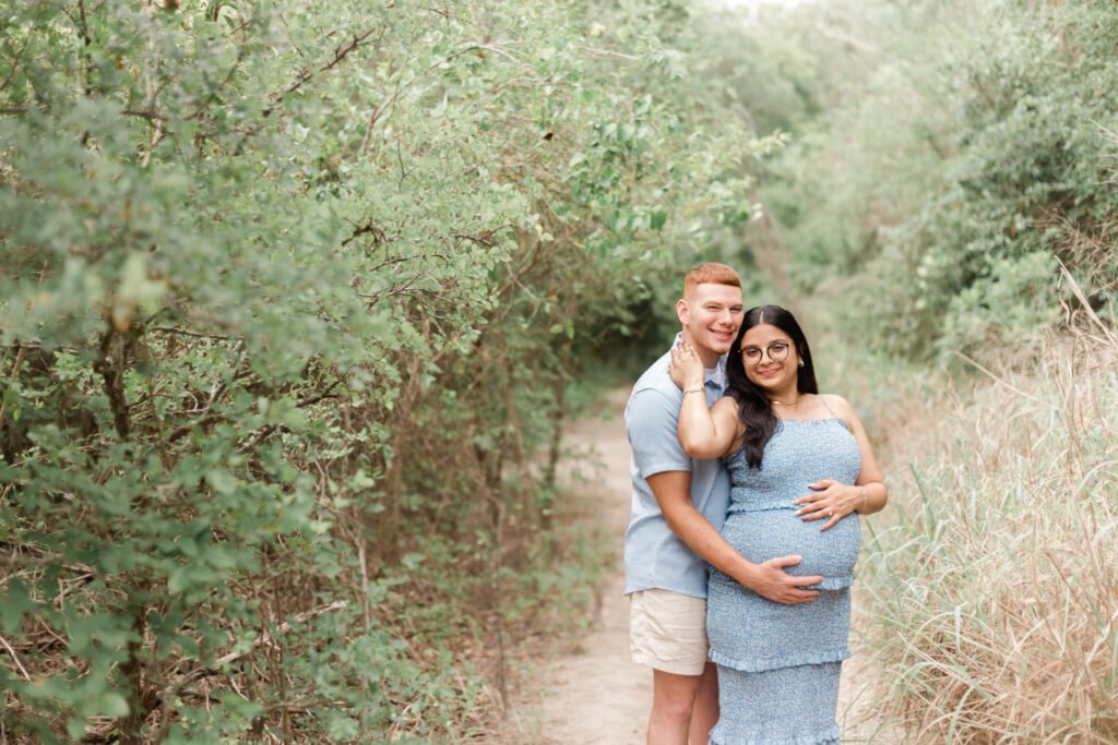 Couple smiles during maternity session along trail