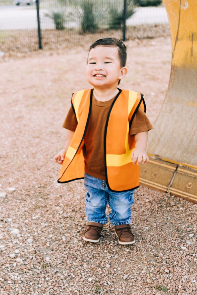 Toddler boy smiling in front of tractor during birthday photoshoot