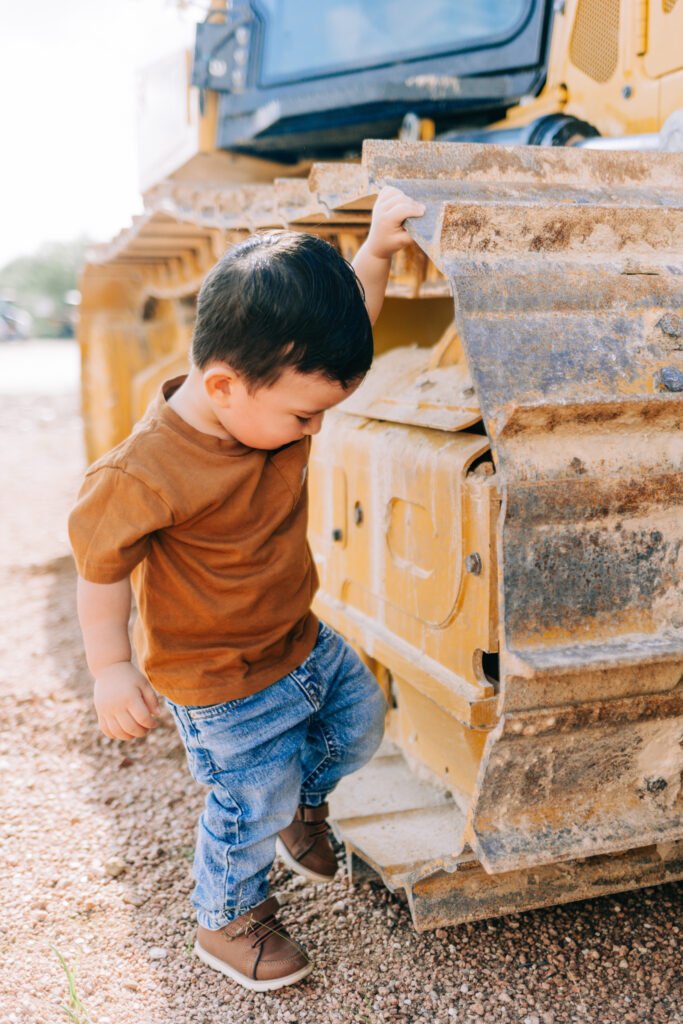Toddler laughing beside wheel of tractor for birthday photoshoot